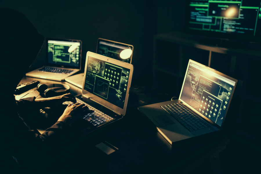 Hacker in a hoodie working in multiple devices in a dark room