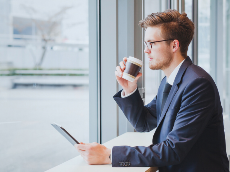 Business man with a coffee and a tablet sitting by a window and looking out