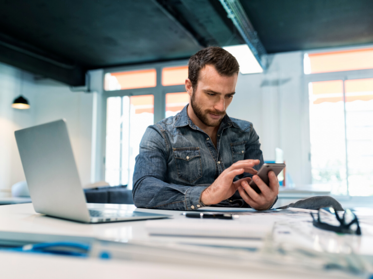 in an office: a man in front of a laptop looking at his smartphone