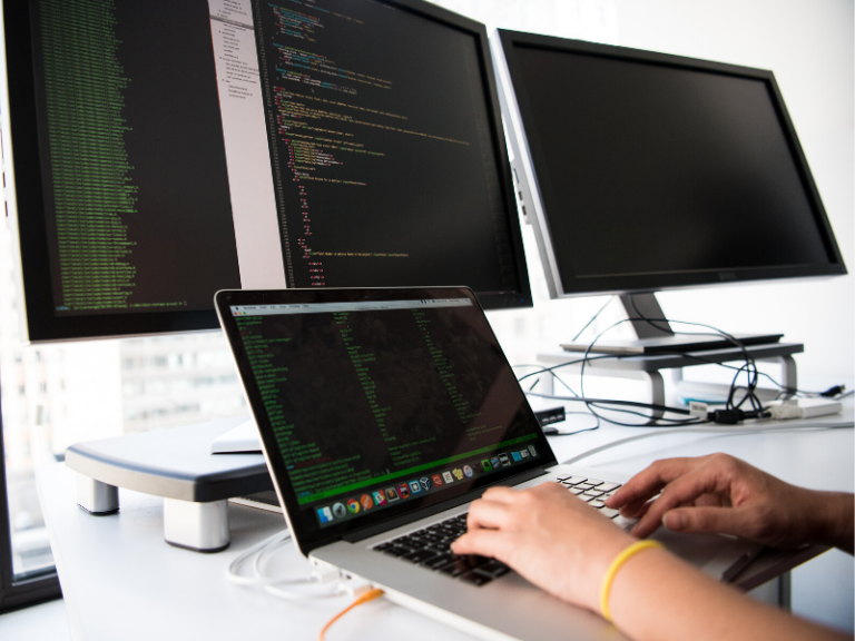 geek writing code on a laptop with three monitors