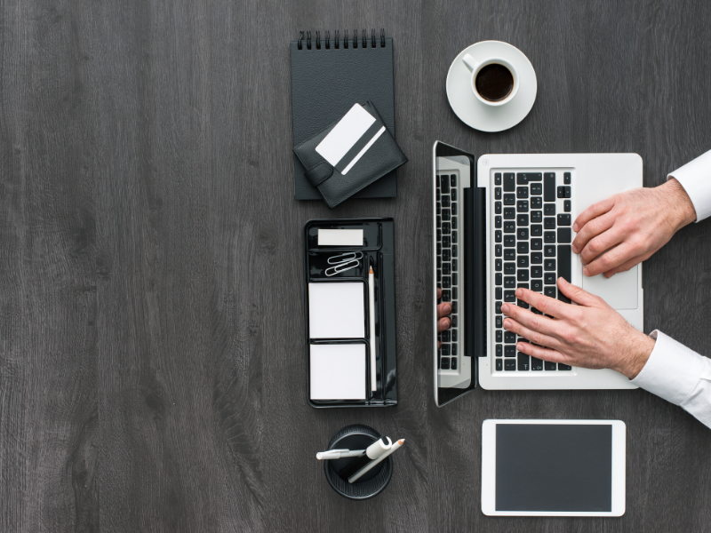 a top view of a table with a laptop, tablet, phone, notebook , a cup of cofee and (most likely) man's hands